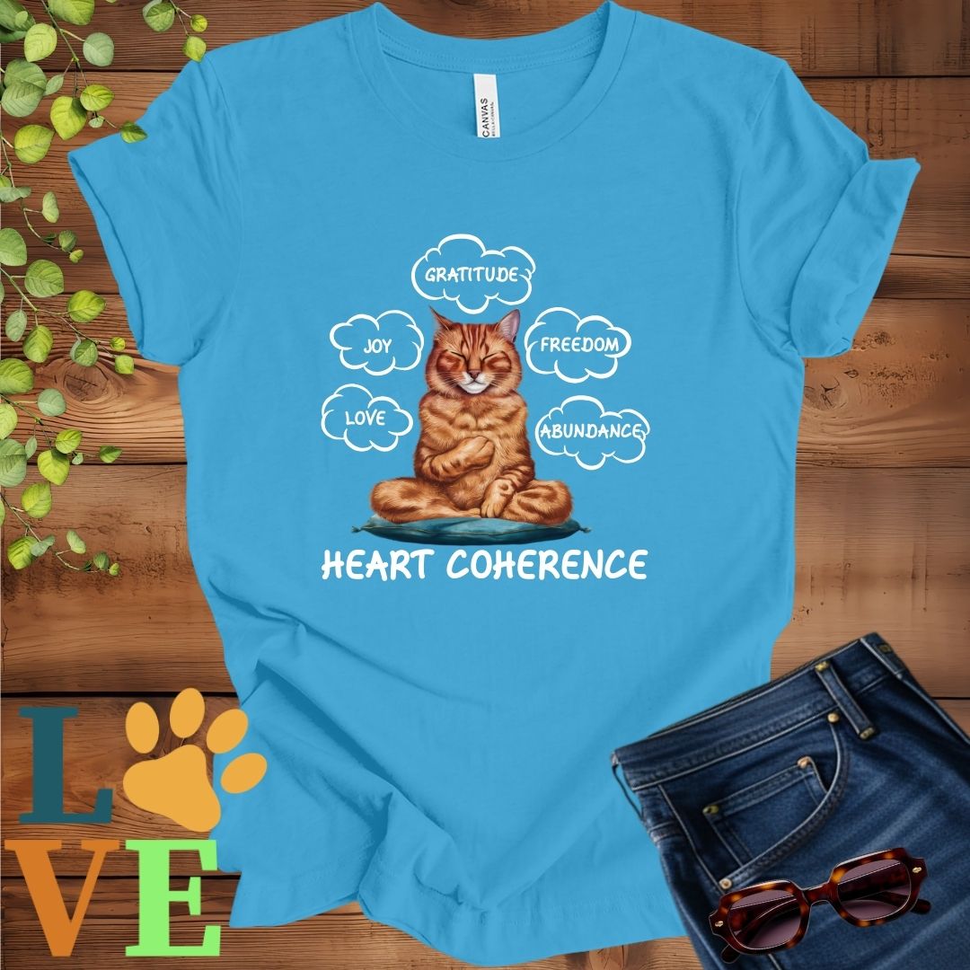 Bright aqua blue t-shirt with a meditating Abyssinian cat, surrounded by floating emotion bubbles labelled love, joy, gratitude, freedom, abundance, and 'Heart Coherence' slogan.