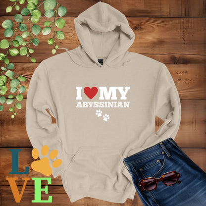 Beige hoodie with 'I ❤️ MY AYSSINIAN' text on a wooden background with green leaves and sunglasses.
