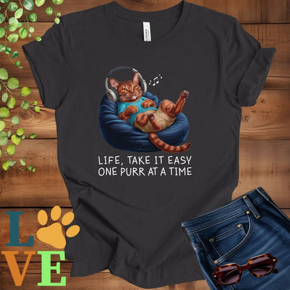 Dark grey heather t-shirt featuring an anthropomorphic Abyssinian cat relaxing on a bean bag while listening to music through headphones, with the slogan "Life, take it easy. One purr at a time."