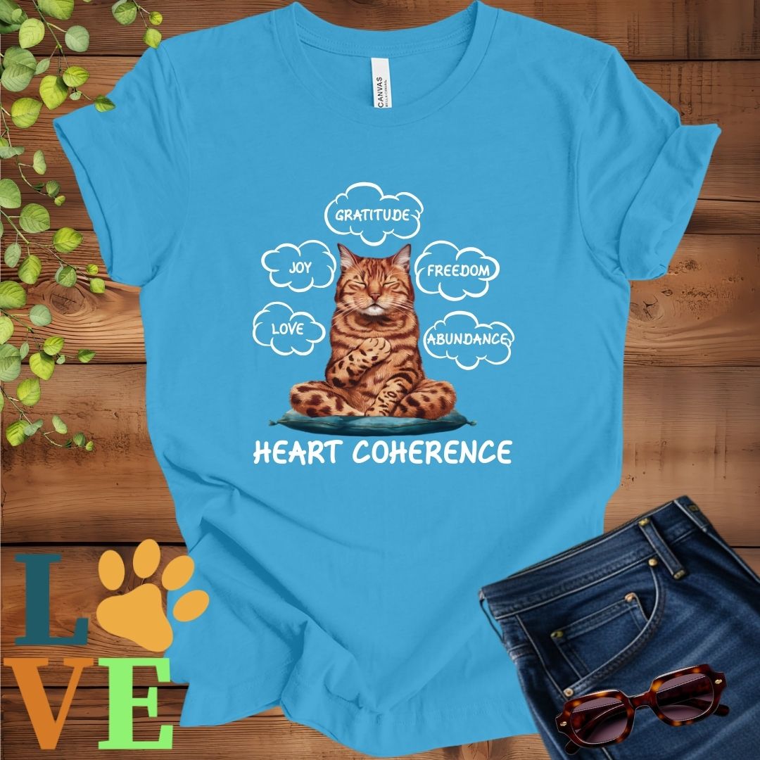 Bright aqua blue t-shirt with a meditating Bengal cat, surrounded by floating emotion bubbles labelled love, joy, gratitude, freedom, abundance, and 'Heart Coherence' slogan.