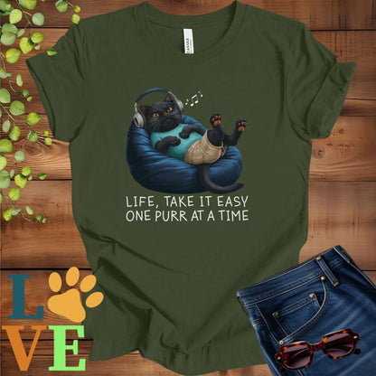 Olive green (military green) t-shirt featuring an anthropomorphic black cat relaxing on a bean bag while listening to music through headphones, with the slogan "Life, take it easy. One purr at a time."
