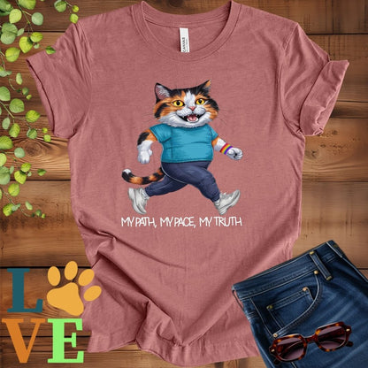 Muted mauve-purple (heather mauve) t-shirt featuring an anthropomorphic calico cat in exercise wear walking confidently with the slogan, "My path, my pace, my truth."
