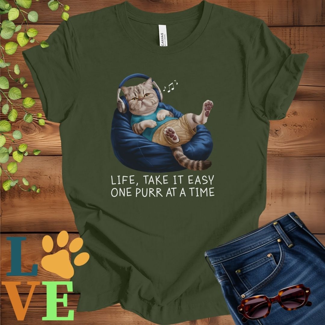 Olive green (military green) t-shirt featuring an anthropomorphic Exotic Shorthair cat relaxing on a bean bag while listening to music through headphones, with the slogan "Life, take it easy. One purr at a time."