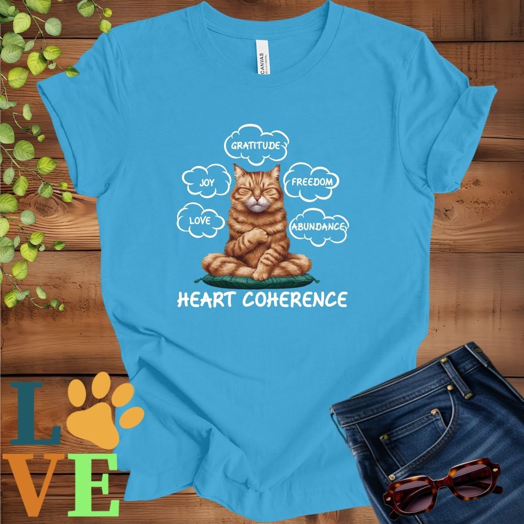Bright aqua blue t-shirt with a meditating ginger cat, surrounded by floating emotion bubbles labelled love, joy, gratitude, freedom, abundance, and 'Heart Coherence' slogan.