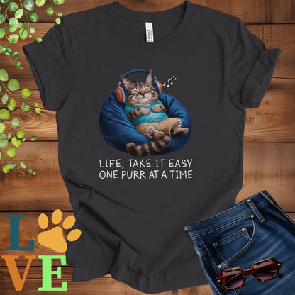 Dark grey heather t-shirt featuring an anthropomorphic Maine Coon cat relaxing on a bean bag while listening to music through headphones, with the slogan "Life, take it easy. One purr at a time."
