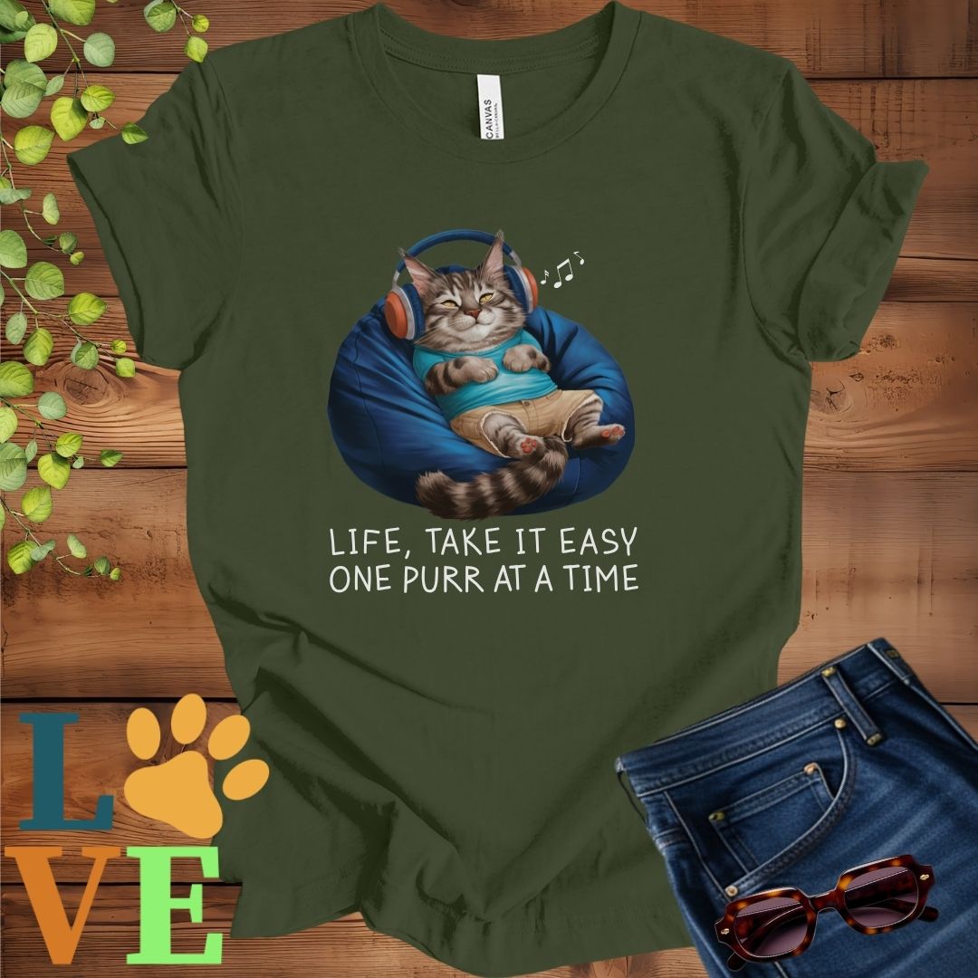 Olive green (military green) t-shirt featuring an anthropomorphic Maine Coon cat relaxing on a bean bag while listening to music through headphones, with the slogan "Life, take it easy. One purr at a time."
