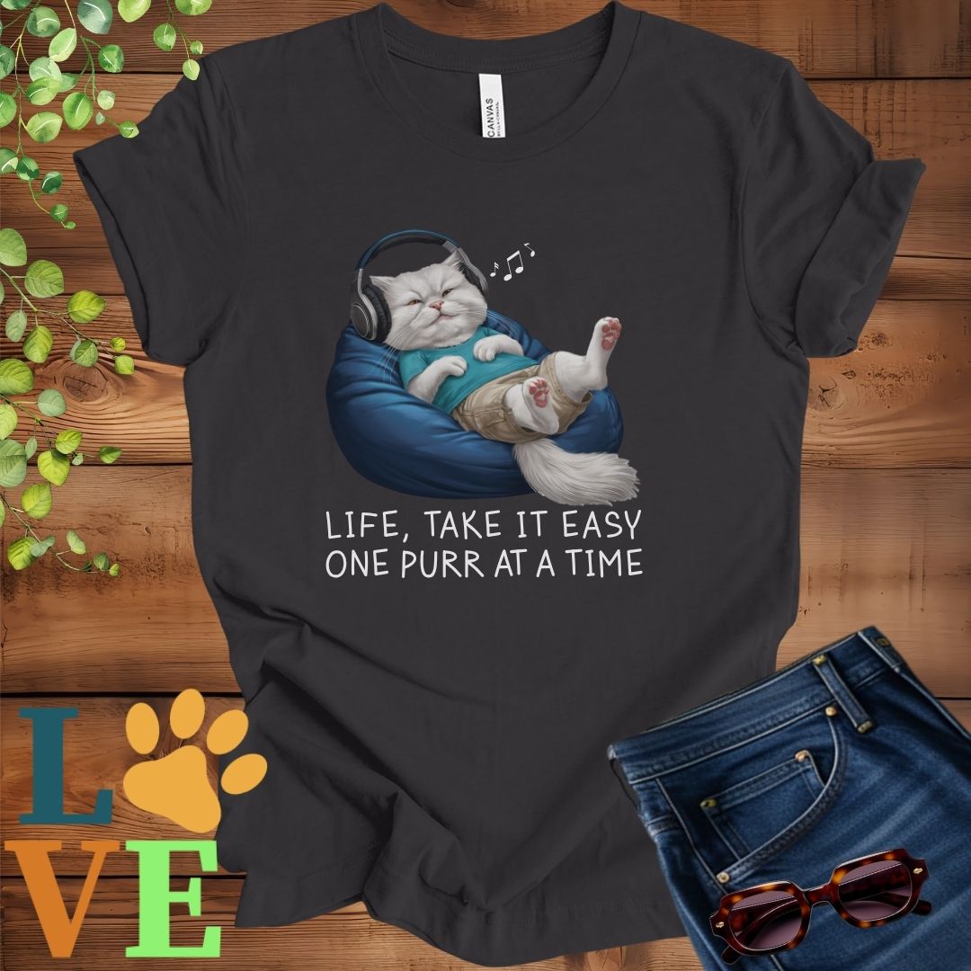 Dark grey heather t-shirt featuring an anthropomorphic Persian cat relaxing on a bean bag while listening to music through headphones, with the slogan "Life, take it easy. One purr at a time."