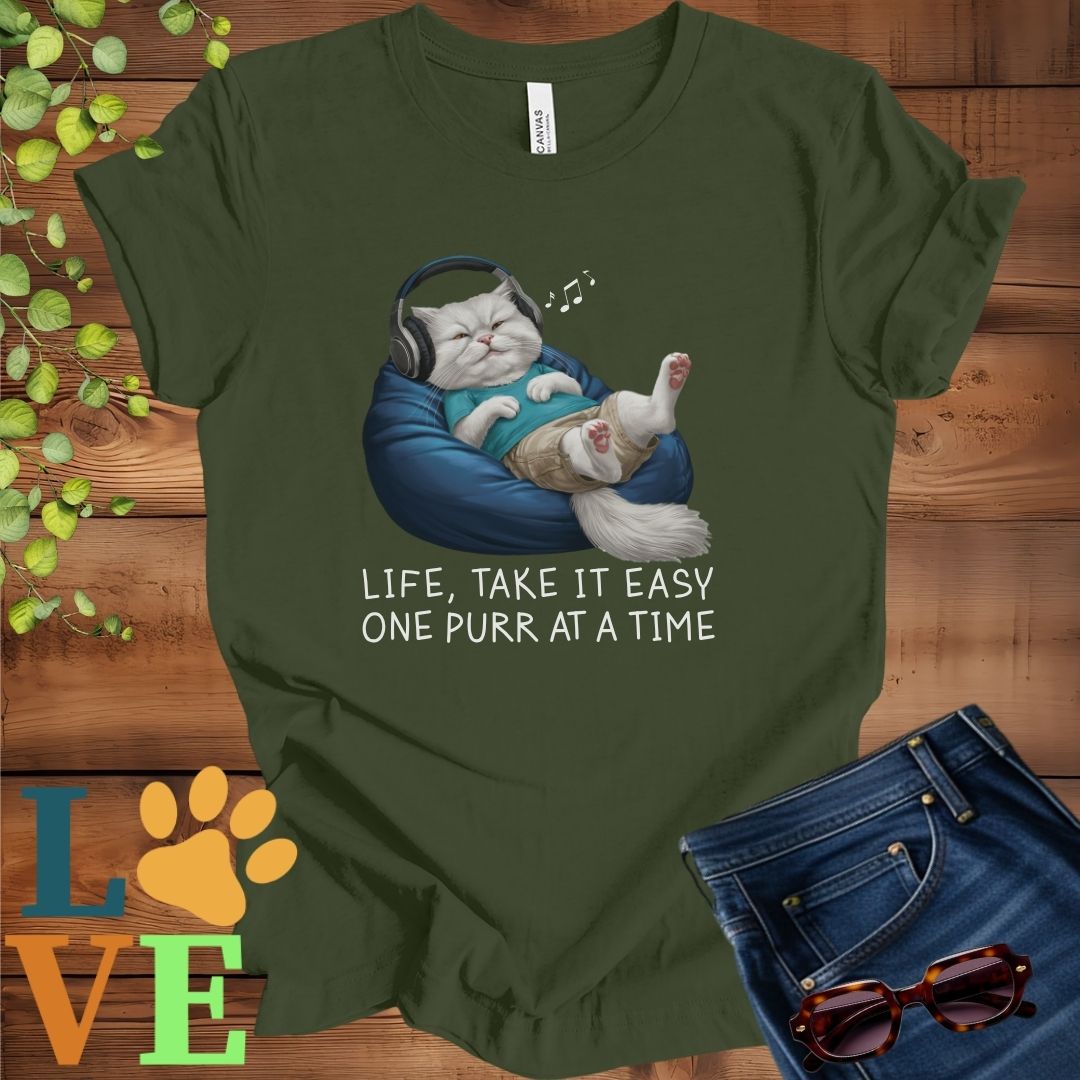 Olive green (military green) t-shirt featuring an anthropomorphic Persian cat relaxing on a bean bag while listening to music through headphones, with the slogan "Life, take it easy. One purr at a time."
