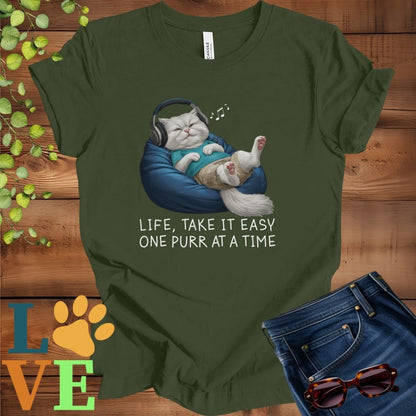 Olive green (military green) t-shirt featuring an anthropomorphic Persian cat relaxing on a bean bag while listening to music through headphones, with the slogan "Life, take it easy. One purr at a time."
