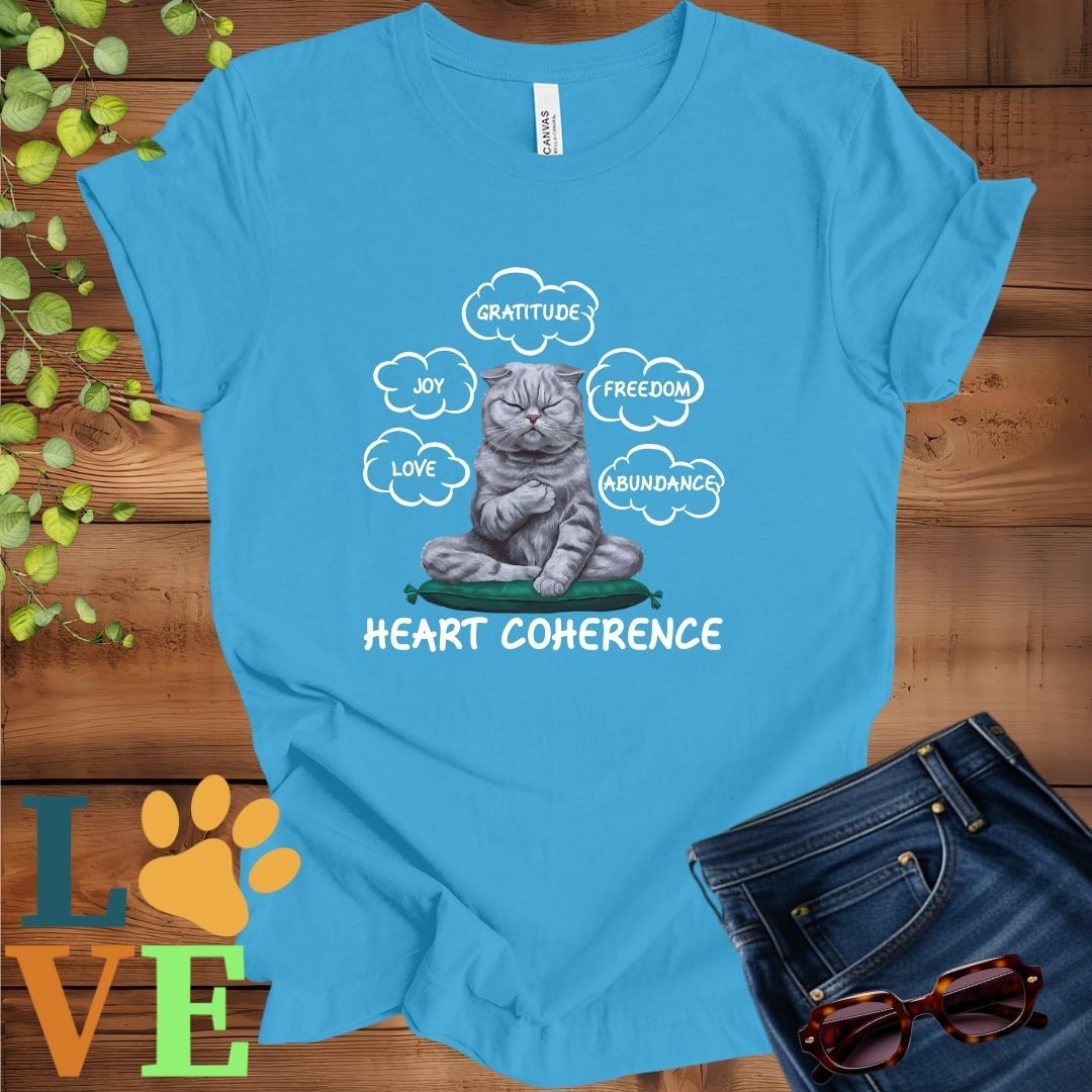 Bright aqua blue t-shirt with a meditating Scottish Fold cat, surrounded by floating emotion bubbles labelled love, joy, gratitude, freedom, abundance, and 'Heart Coherence' slogan.