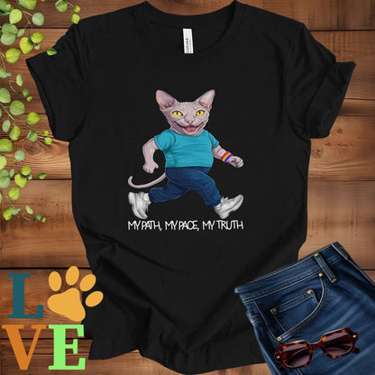 Black t-shirt featuring an anthropomorphic Sphynx cat in exercise wear walking confidently with the slogan, "My path, my pace, my truth."
