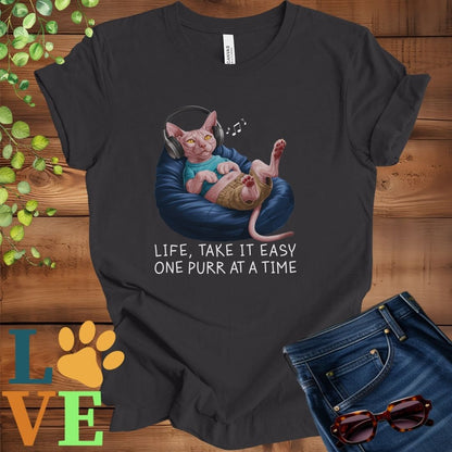Dark grey heather t-shirt featuring an anthropomorphic Sphynx cat relaxing on a bean bag while listening to music through headphones, with the slogan "Life, take it easy. One purr at a time."
