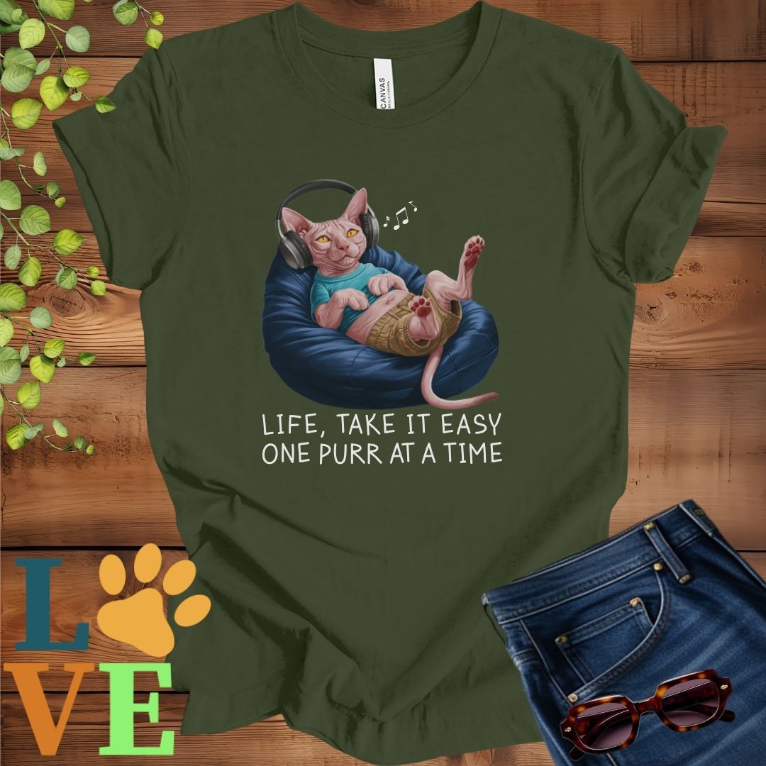 Olive green (military green) t-shirt featuring an anthropomorphic Sphynx cat relaxing on a bean bag while listening to music through headphones, with the slogan "Life, take it easy. One purr at a time."