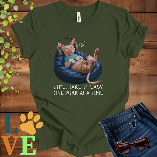 Olive green (military green) t-shirt featuring an anthropomorphic Sphynx cat relaxing on a bean bag while listening to music through headphones, with the slogan "Life, take it easy. One purr at a time."